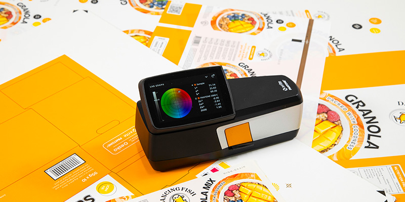 An eXact 2 handheld spectrophotometer sitting on printed material for color assessment